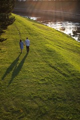 Young couple is walking along the river bank at sunset.