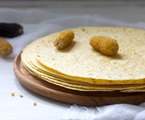 A stack of round corn tortillas on a wooden board and corncobs.