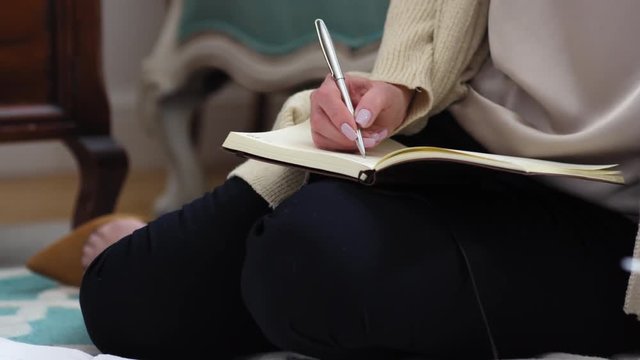 Close up of woman sitting on floor with notebook on her knees and making notes in it