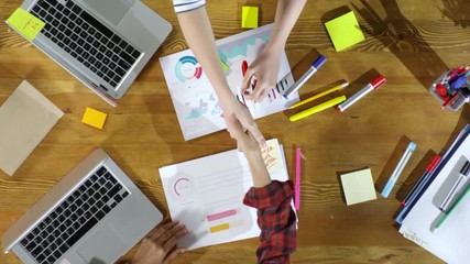 Directly above view of handshake of two female hands and wooden table with laptops