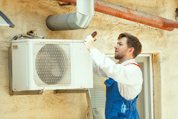 HVAC technician working on a capacitor part for condensing unit. Male worker or repairman in uniform repairing and adjusting conditioning system, diagnosting and looking for technical issues.