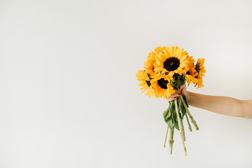 Women's hand hold yellow sunflowers bouquet on white background. Summer floral concept.
