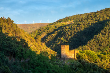 View of Lousã Castle on a late spring afternoon, lit by the sunset with the serra da Lousã, Talasnal village and wind turbines in the background.