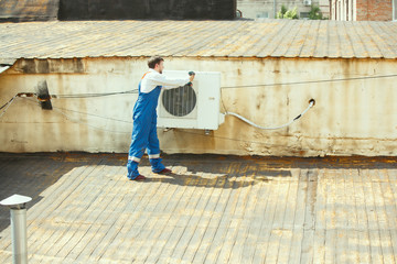 HVAC technician working on a capacitor part for condensing unit. Male worker or repairman in uniform repairing and adjusting conditioning system, diagnosting and looking for technical issues.