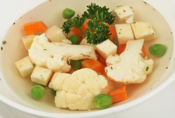 Vegetable soup with cauliflower, potatoes, peas, carrots and parsley on a white isolated background