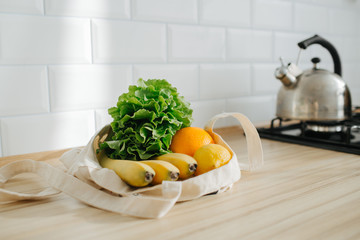 Lettuce, lemon, banana and orange in a white cotton bag in the sunny kitchen, lying on the table.
