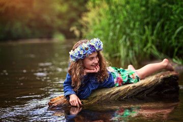 girl in curly hair in a wreath lies on the river