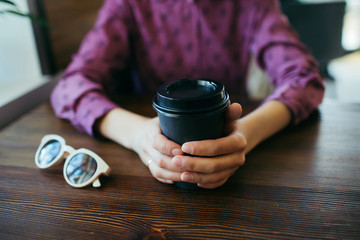Closeup of woman's hands, holding a black cup with coffee in a cafe. Friendly chat.