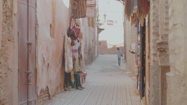 Dusty street in a Moroccan alleyway with shop fronts selling colorful items on a hot and sunny day