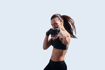 Boxing power. Attractive young woman looking at camera and boxing while standing against grey...