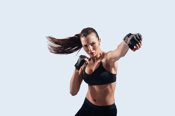 Full of strength. Attractive young woman looking at camera and boxing while standing against grey...