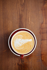 A cup of delicious cappucino in a red mug. Top view above the wooden table.