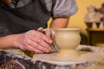 Professional potter carving mug with special tool in pottery workshop