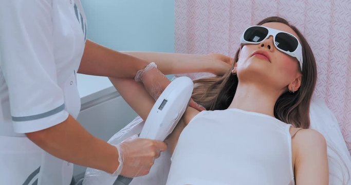 Medium shot of young slim brunette woman while laser armpit hair removal procedure. Unwanted hair concept
