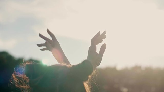 Rear view of woman with hands raised dancing outdoors