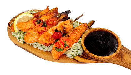 Grilled salmon skewers with rice on an olive wood serving board isolated on a white background