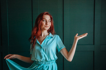 Red-haired girl in blue dress shows hand. on a dark green background. copy space