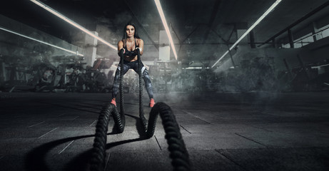 Sport backgrounds. Powerful attractive muscular woman fitness trainer do battle workout with ropes...