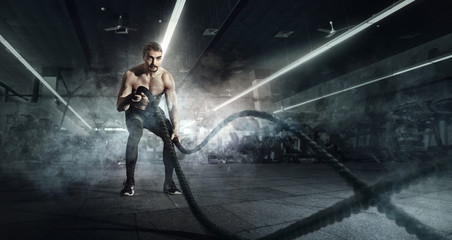 Sport. Strong man exercising with battle ropes at the gym with. Athlete doing battle rope workout at gym. Dramatic sports background.