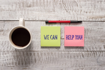Text sign showing We Can Help You. Business photo text offering good assistance to customers or friends Stationary placed next to a cup of black coffee above the wooden table