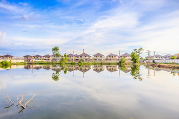 Fototapeta premium New house building reflection with water in lake at residential estate construction site with clouds and blue sky