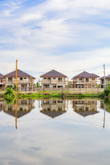 Fototapeta na wymiar New house building reflection with water in lake at residential estate construction site with clouds and blue sky