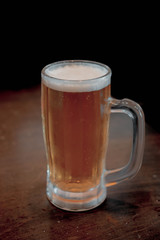frosted mug filled with a golden amber ale beer on a wooden table. dark room
