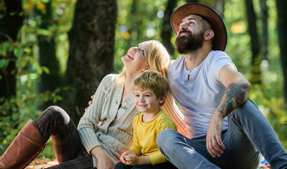 Fototapeta premium Family day concept. Happy family with kid boy relaxing while hiking in forest. Family weekend. Mother father and little son sit forest picnic. Good day for spring picnic in nature. United with nature