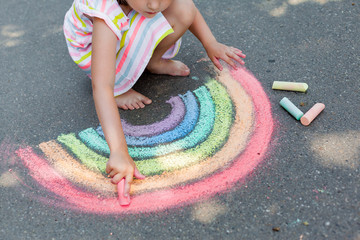 the child girl draws a rainbow with colored chalk on the asphalt. Child drawings paintings concept. Education and arts, be creative when back to school  - obrazy, fototapety, plakaty