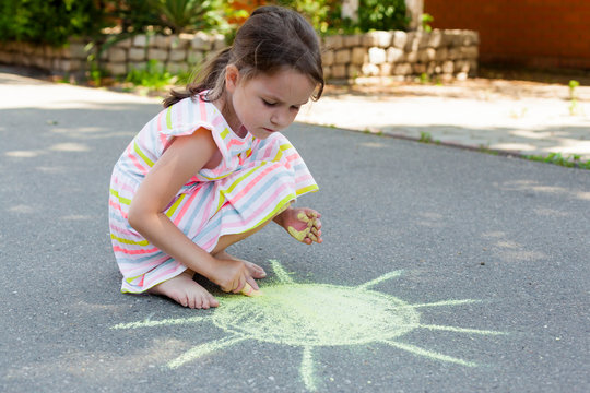 a child draws with chalk the sun on the pavement. Summer outdoor activity concept, drawing with chalks on asphalt