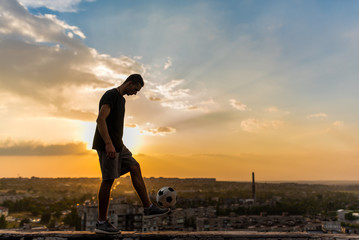 Man playing with ball outdoors on the roof on the background of the city and sunset