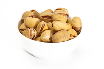 Fried salted pistachios in a ceramic bowl on a white background