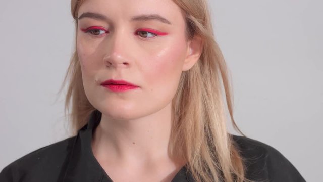 blonde woman with bright red eyewing makeup looking straight to the camera Slow motion blowing hair