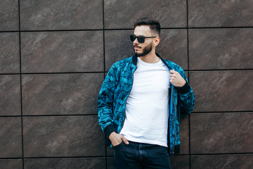 A young stylish man with a beard in a white T-shirt and glasses. Street photo