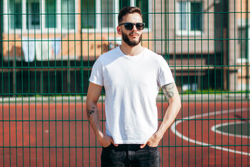 A young stylish man with a beard in a white T-shirt and glasses. Street photo