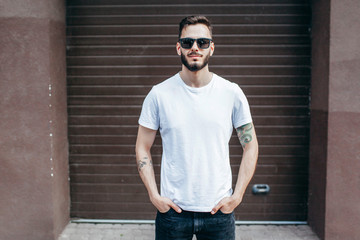 A young stylish man with a beard in a white T-shirt and glasses. Street photo