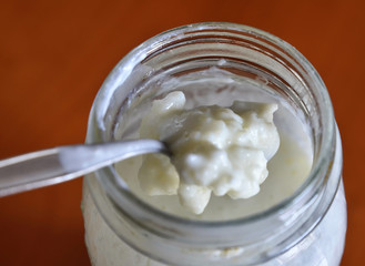 A teaspoon stirs the kefir and raises some granules in a close-up shot