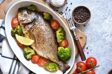 Baked dorado with spices, with broccoli and tomatoes on a concrete background.
