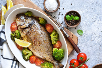 Baked dorado with spices, with broccoli and tomatoes on a concrete background.