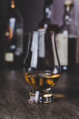 Whisky glass with single malt scotch on wooden table and scotch bottles on the background
