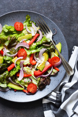 Vegan salad cabbage, spinach, tomatoes, peppers, avocados, onions with olive oil on the kitchen table. View from above.