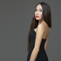 Young brunette woman with red lipstick and long straight hair. Black open dress.