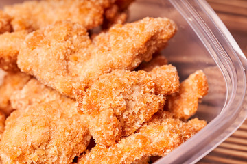 Chicken strips in a plastic container on a wooden table.