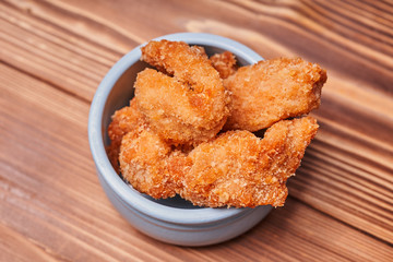 Chicken strips in a clay pot on a wooden table.