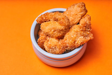 Chicken strips in a clay pot on an orange background.