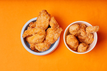Chicken strips in a clay pot on an orange background.