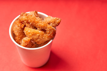 Chicken strips in a paper Cup on a red background.