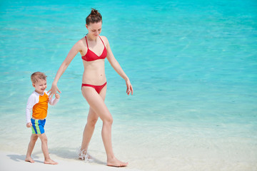 Naklejka premium Three year old toddler boy walking on beach with mother. Summer family vacation at Maldives.