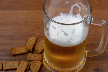 A glass of light beer with crackers on a wooden table