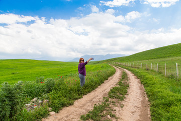 A plus-size girl is walking along the side of a country road. Spring landscape, green hills, blue sky.